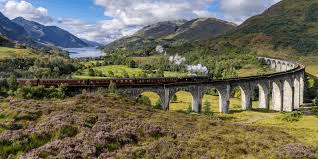 Steam train crossing Glenfinnan Viaduct with mountains and loch in the Scottish Highlands
